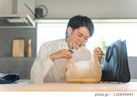 帰宅後ダイニングでコンビニ弁当を開けるスーツ姿のアジア人ビジネスマン男性 帰宅後ダイニングでコンビニ弁当を開けるスーツ姿のアジア人ビジネスマン男性 116694845