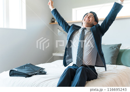 ベッドに座る疲れたスーツ姿の若いビジネスマン（飲み過ぎ・二日酔い・朝帰り・酔っ払い） 116695243