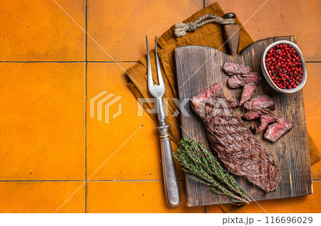 Grilled Medium Rare Machete or skirt beef meat steak on wooden cutting board. Orange background. Top view. Copy space 116696029