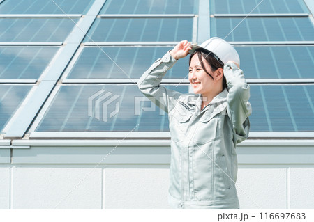 太陽光発電・ソーラーパネルの前に立つ電力会社・電気工事業者の作業着姿の技術者・ビジネスパーソン 116697683