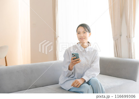 部屋のソファでスマホを操作する女性 部屋のソファでスマホを操作する女性 116699306