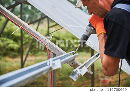 Worker fixing metal beams with electric drill for solar panels. Concept of renewable and ecological energy. Modern technology and innovation. Idea of environment safe. European man wear workwear 116700669