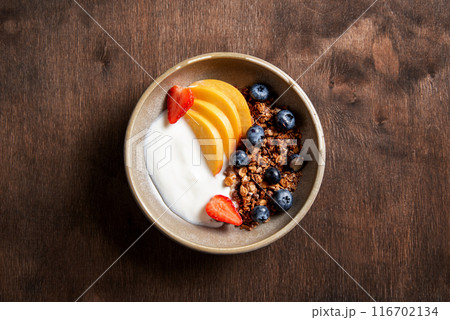 Fresh natural yogurt with homemade granola, peach, strawberry and blueberry in a bowl  116702134