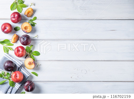 concept flat lay a few juicy red plums with branch blossom flowers  on a white wood background.  116702159