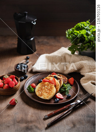 Cottage cheese pancakes or syrniki  with mint, strawberries and blueberries on a dark wooden table  116703116