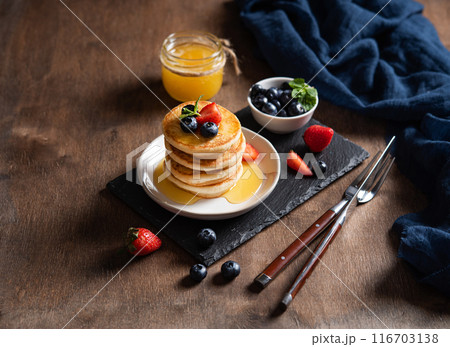 Delicious homemade pancakes with strawberries and blueberries and honey on a dark wooden background  116703138
