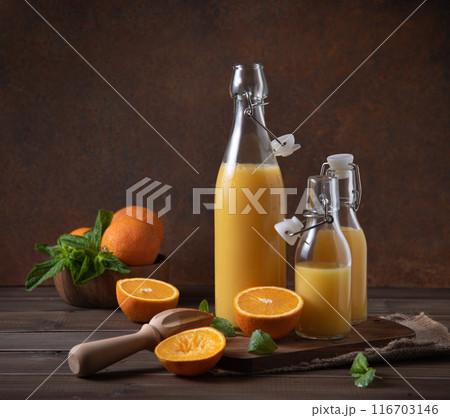 freshly squeezed orange juice in three bottles with citrus fruits on cutting board and  116703146