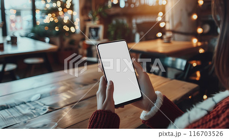 womans hands holding smartphone in rustic cafe blank white screen mockup wooden table background warm ambient lighting 116703526