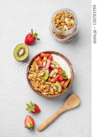 Natural yogurt with granola, kiwi and strawberries in a wooden bowl on a light background 116703768