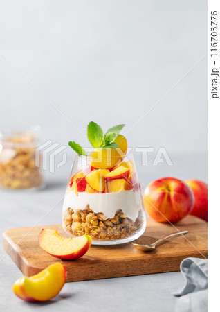 Greek yogurt parfait with peach and granola in a glass on a wooden board on a light background 116703776