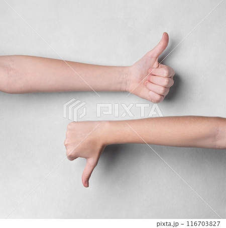 Two hands showing thumbs up and thumbs down gestures on a light background. 116703827
