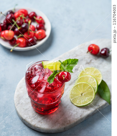 Cherry-lime mojito cocktail with mint, lime and ice on a marble board on a blue background. Cherry-lime mojito cocktail with mint, lime and ice on a marble board on a blue background. 116704003