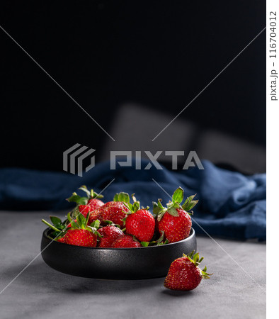 Strawberries in a black bowl on a dark background with a napkin and shadows. Strawberries in a black bowl on a dark background with a napkin and shadows. 116704012