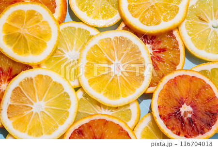 Slices of lemons and blood oranges close up on a blue background. 116704018