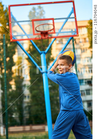 caucasian little basketball player jumps to throw the ball into the basket hoop 116704048