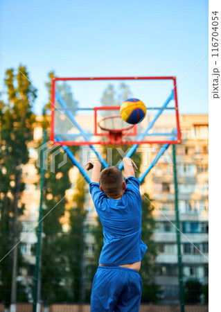 caucasian little basketball player jumps to throw the ball into the basket hoop 116704054