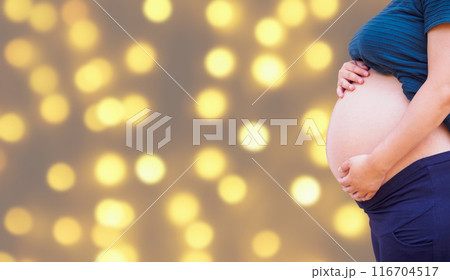 pregnant woman holding her pregnant belly over holiday bokeh lights background 116704517