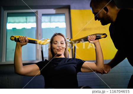 Personal coach assisting sportswoman in using machine 116704655