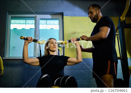 Personal coach assisting sportswoman in using machine Personal coach assisting sportswoman in using machine 116704661