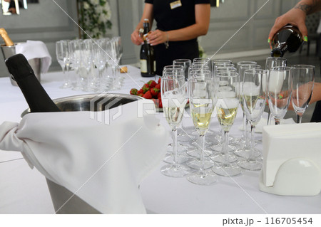 The waiter pours champagne into glasses. Champagne on the table at the restaurant. 116705454