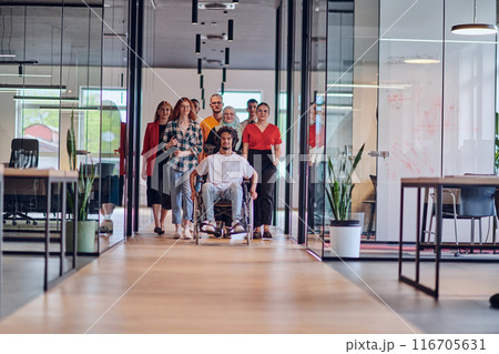 A diverse group of young business people congregates within a modern startup's glass-enclosed office, featuring inclusivity with a person in a wheelchair, an African American young man , and a hijab 116705631