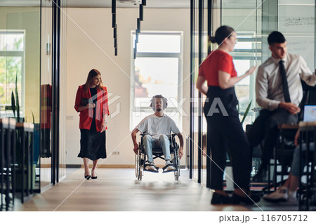 A group of young business people in a modern glass-walled office captures the essence of diversity and collaboration, while two colleagues, including an African American businessman in a wheelchair A group of young business people in a modern glass-walled office captures the essence of diversity and collaboration, while two colleagues, including an African American businessman in a wheelchair 116705712