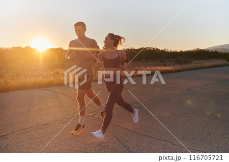 A handsome young couple running together during the early morning hours, with the mesmerizing sunrise casting a warm glow, symbolizing their shared love and vitality 116705721