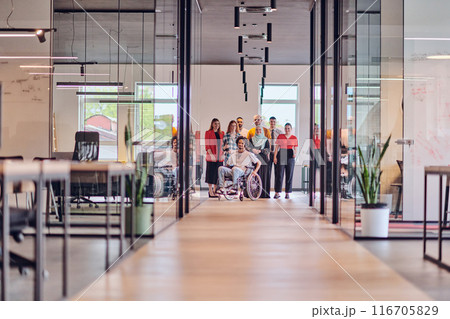 A diverse group of young business people congregates within a modern startup's glass-enclosed office, featuring inclusivity with a person in a wheelchair, an African American young man , and a hijab 116705829