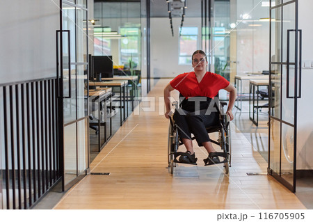 A modern young businesswoman in a wheelchair is surrounded by an inclusive workspace with glass-walled offices, embodying determination and innovation in the business world 116705905