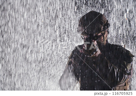 Army soldier in Combat Uniforms with an assault rifle, plate carrier and combat helmet going on a dangerous mission on a rainy night. 116705925