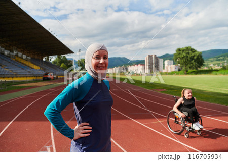 A Muslim woman wearing a burqa resting with a woman with disability after a hard training session on the marathon course 116705934
