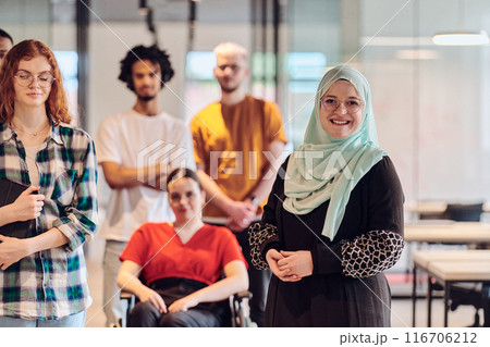 A diverse group of young business people congregates within a modern startup's glass-enclosed office, featuring inclusivity with a person in a wheelchair, an African American young man , and a hijab 116706212