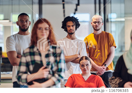 A diverse group of business people walking a corridor in the glass-enclosed office of a modern startup, including a person in a wheelchair and a woman wearing a hijab, showing a dynamic mix of 116706385