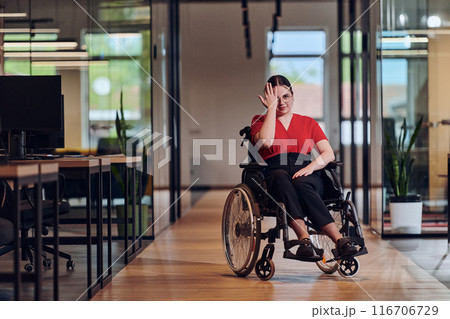 A modern young businesswoman in a wheelchair is surrounded by an inclusive workspace with glass-walled offices, embodying determination and innovation in the business world A modern young businesswoman in a wheelchair is surrounded by an inclusive workspace with glass-walled offices, embodying determination and innovation in the business world 116706729