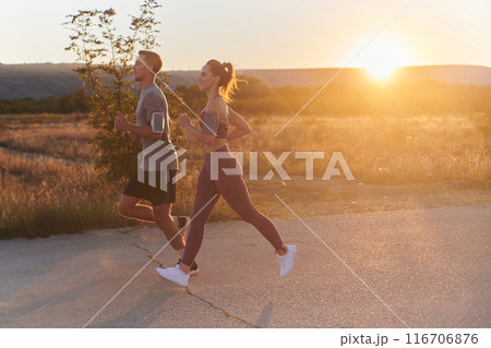 A handsome young couple running together during the early morning hours, with the mesmerizing sunrise casting a warm glow, symbolizing their shared love and vitality 116706876