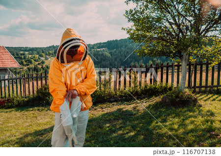 Beekeeper put on a protective beekeeping suit and preparing to enter the apiary Beekeeper put on a protective beekeeping suit and preparing to enter the apiary 116707138