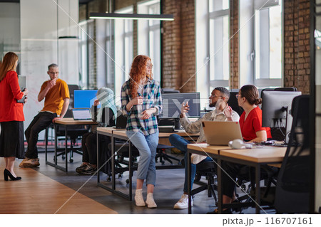 A diverse group of young business individuals congregates in a modern startup coworking center, embodying collaborative innovation and a dynamic atmosphere. 116707161