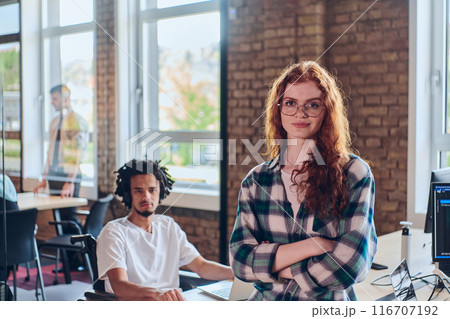 A portrait of a young businesswoman with modern orange hair captures her poised presence in a hallway of a contemporary startup coworking center, embodying individuality and professional confidence. 116707192