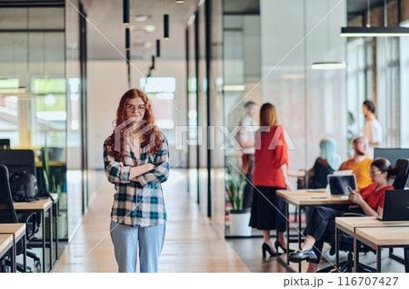 A portrait of a young businesswoman with modern orange hair captures her poised presence in a hallway of a contemporary startup coworking center, embodying individuality and professional confidence. A portrait of a young businesswoman with modern orange hair captures her poised presence in a hallway of a contemporary startup coworking center, embodying individuality and professional confidence. 116707427