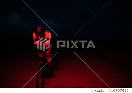 A triathlete rides his bike in the darkness of night, pushing himself to prepare for a marathon. The contrast between the darkness and the light of his bike creates a sense of drama and highlights the 116707435