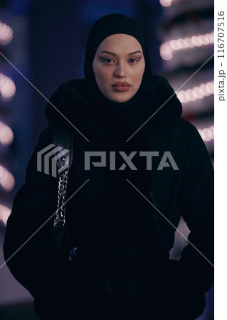 Muslim woman walking on an urban city street on a cold winter night wearing hijab 116707516