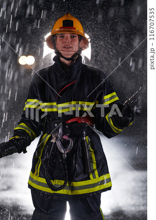A determined female firefighter in a professional uniform striding through the dangerous, rainy night on a daring rescue mission, showcasing her unwavering bravery and commitment to saving lives. 116707535