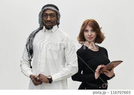 Arabic entrepreneur and a businesswoman, exuding confidence and unity, pose together against a clean white backdrop, symbolizing a dynamic partnership characterized by ambition, innovation, and 116707603