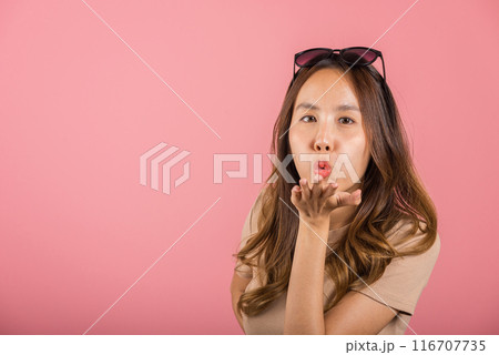Asian happy portrait beautiful cute young woman teen standing blowing kiss air something on palm hands expresses her love looking to camera studio shot isolated on pink background with copy space 116707735