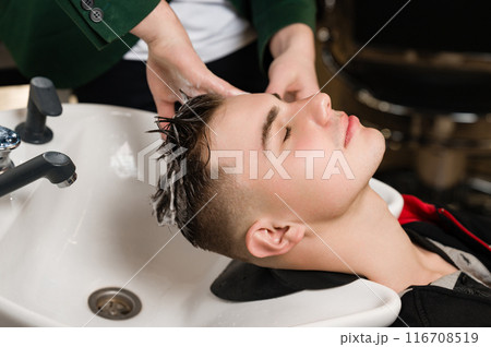 Barber shampooing washing a male clients head in the sink. 116708519