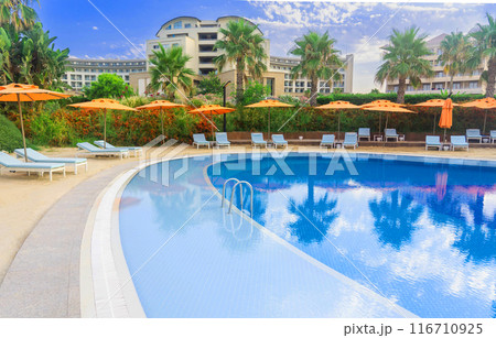 A beautiful luxury hotel pool with a strip of coastal sand and colorful umbrellas and sun loungers A beautiful luxury hotel pool with a strip of coastal sand and colorful umbrellas and sun loungers 116710925