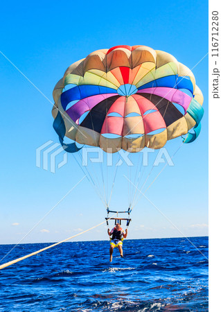 Parasailing water amusement - flying on a parachute behind a boat on a summer holiday by the sea. Summer vacation concept Parasailing water amusement - flying on a parachute behind a boat on a summer holiday by the sea. Summer vacation concept 116712280