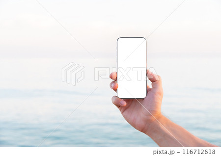 Close-up white screen Caucasian man holding a regular smartphone in his left hand, ocean beach in the background. High quality photo. Smartphone screen mockup cut out Close-up white screen Caucasian man holding a regular smartphone in his left hand, ocean beach in the background. High quality photo. Smartphone screen mockup cut out 116712618