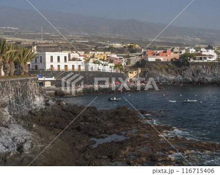 Views of the picturesque Alcala village with traditional architecture houses, small tranquil cove with beach and pier crowded with sunbathing people. Tenerife, Canary Islands, Spain. 116715406