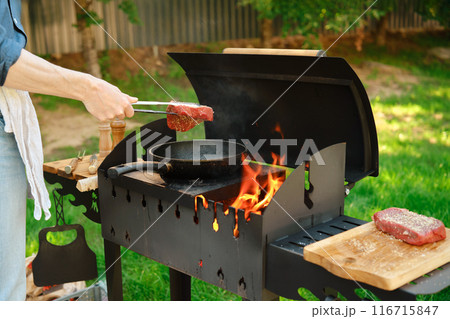 Unrecognizable man puts a steak on a frying pan with kitchen tongs Unrecognizable man puts a steak on a frying pan with kitchen tongs 116715847
